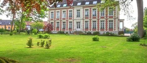 A large, multi-story building with a symmetrical facade, surrounded by a well-maintained lawn and trees.