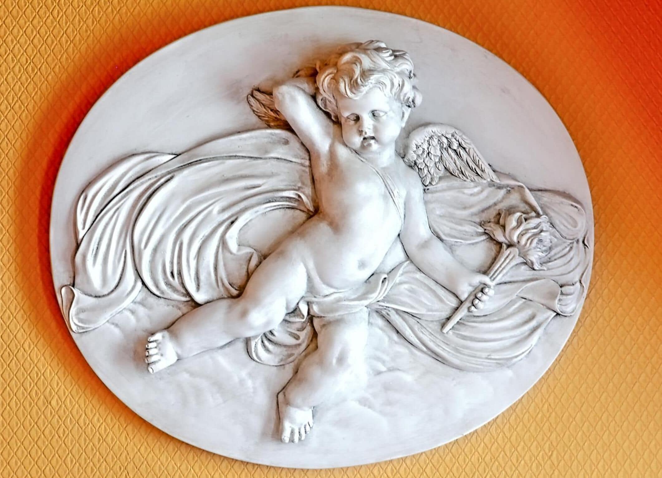 A detailed sculpture of a cherub with wings and a flower, placed on a textured surface.