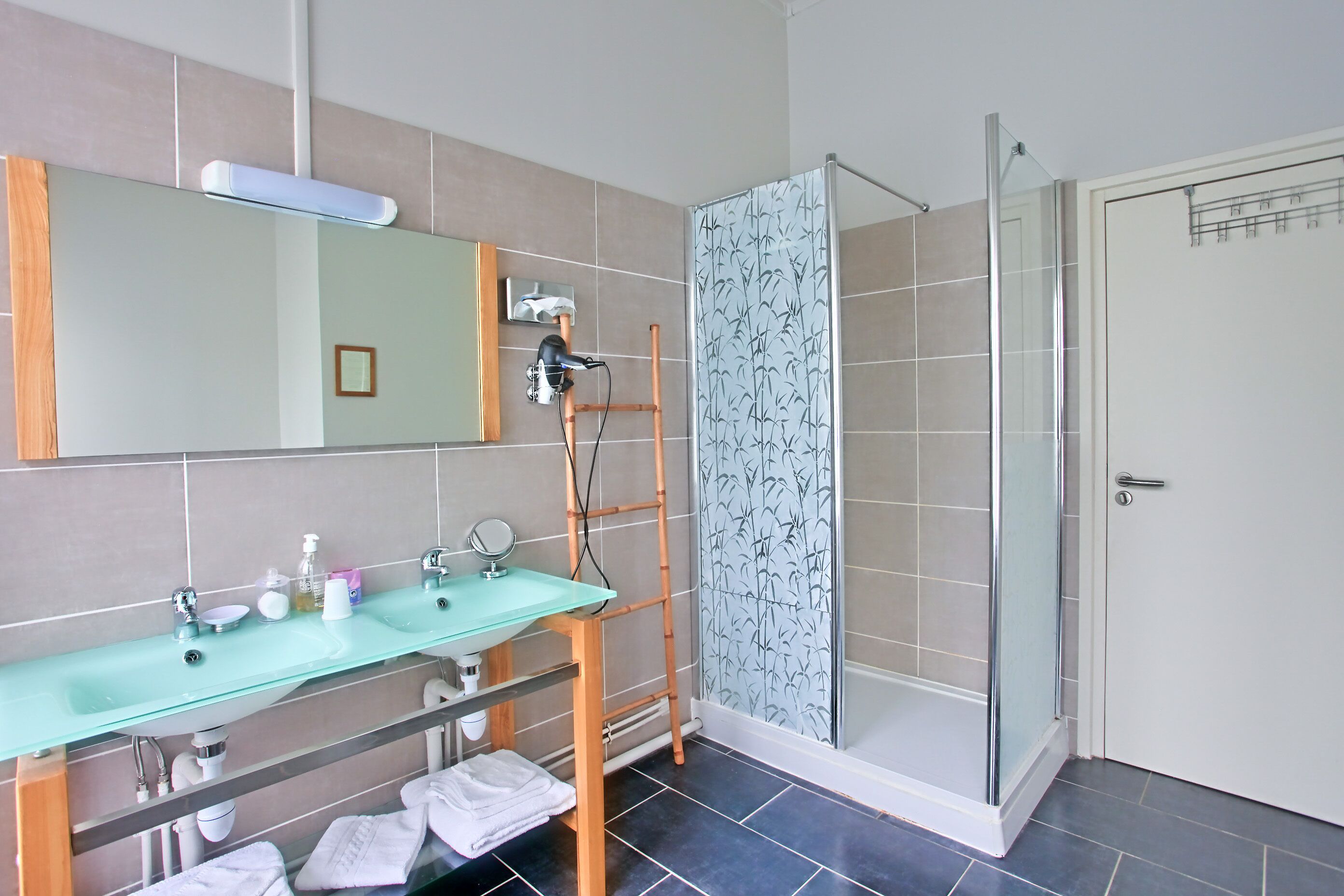 Baño con lavamanos de vidrio, espejo y ducha con escalera de bambú.