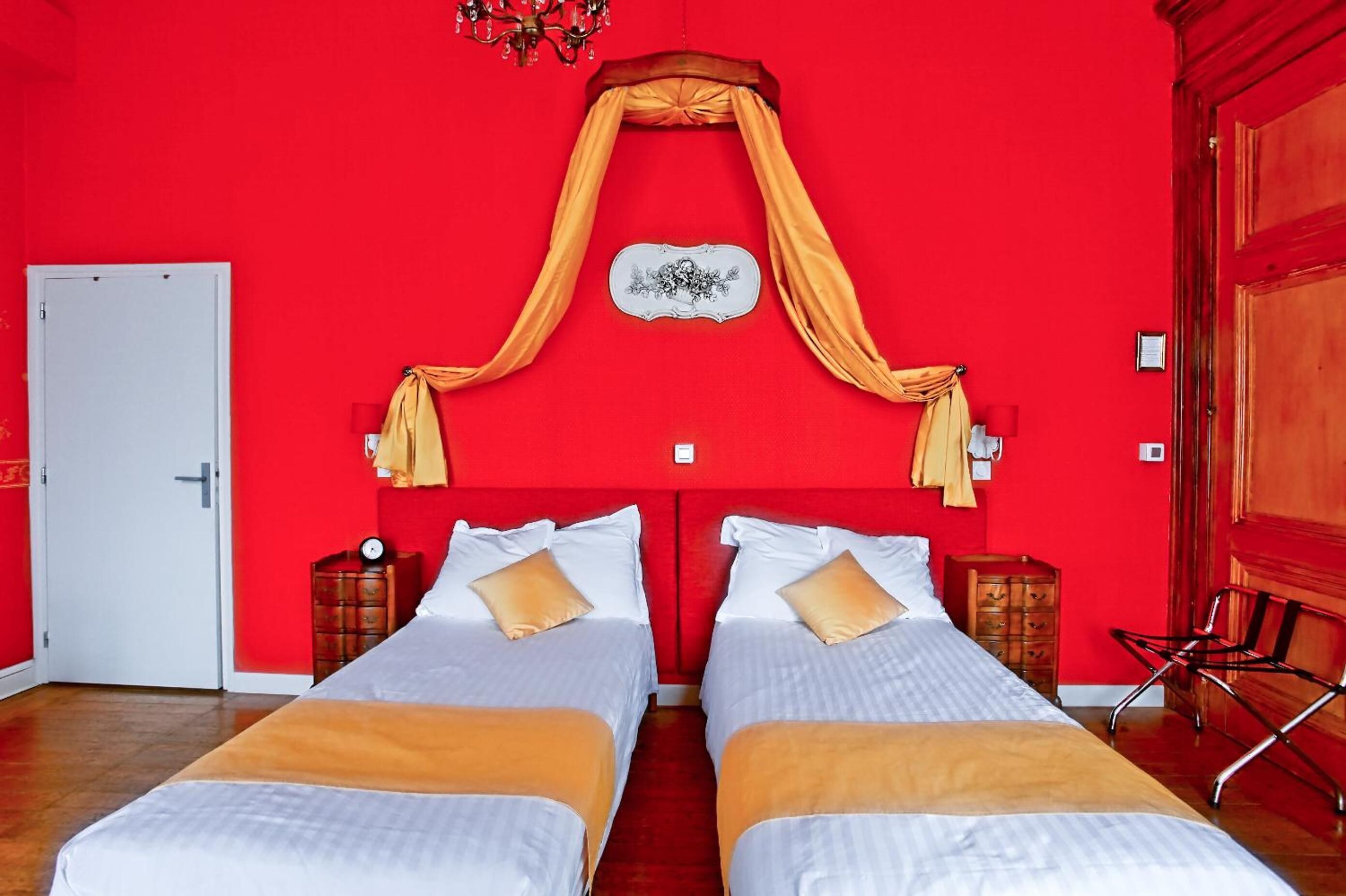A room with two beds, red walls, a chandelier, and a decorative wall piece.