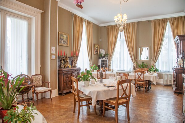 Une salle à manger avec des meubles en bois, un lustre et de grandes fenêtres ornées de rideaux.