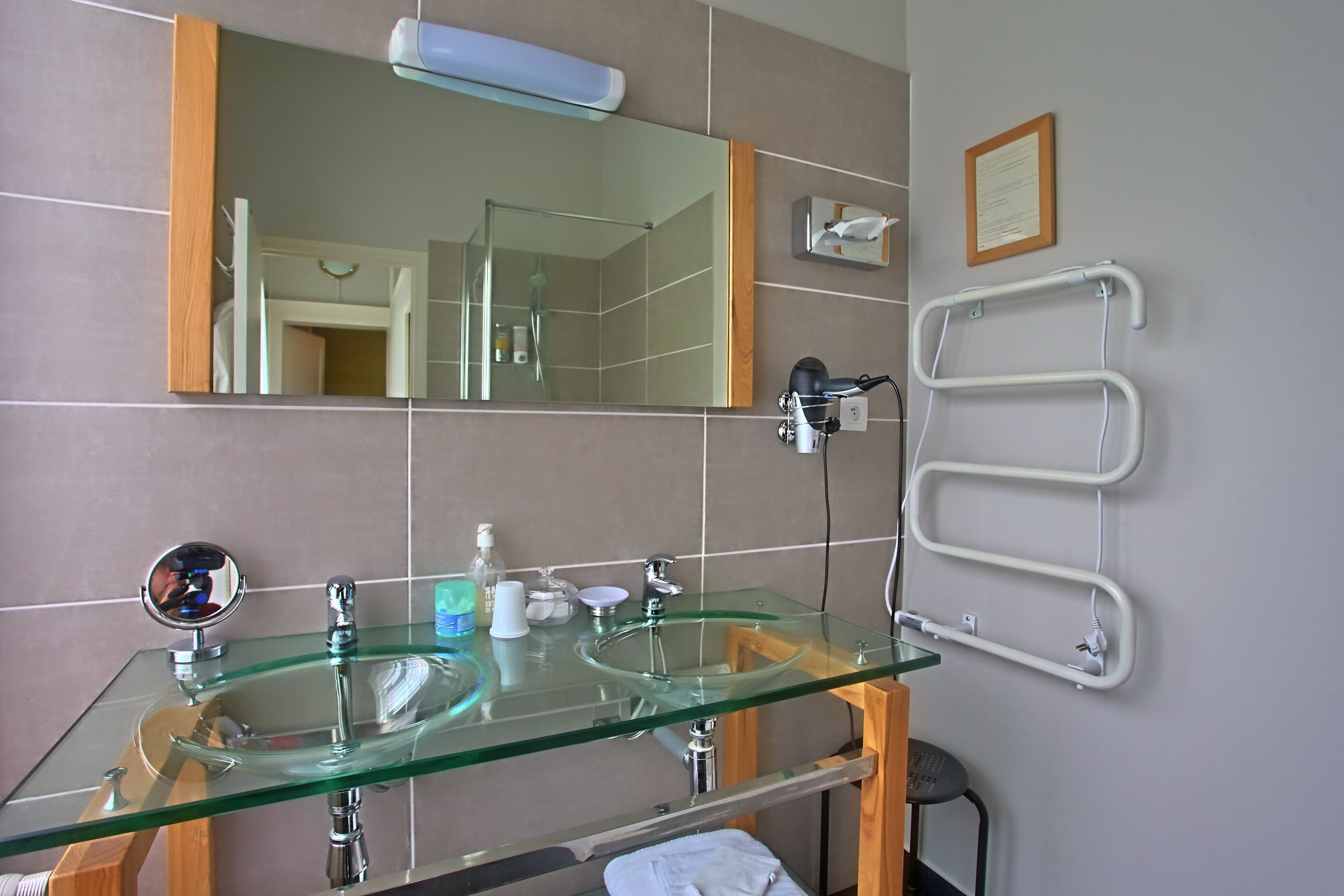 Un baño con un lavabo de vidrio, un espejo, un perchero para toallas y un aviso en un marco en la pared.