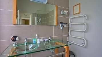 Un baño con un lavabo de vidrio, un espejo, un perchero para toallas y un aviso en un marco en la pared.