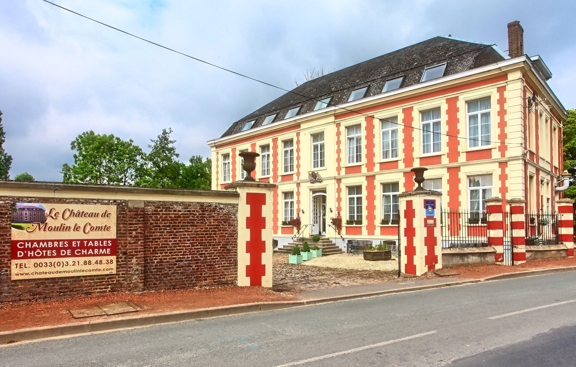 A historic building with a red and cream facade, large windows, and a brick wall entrance.