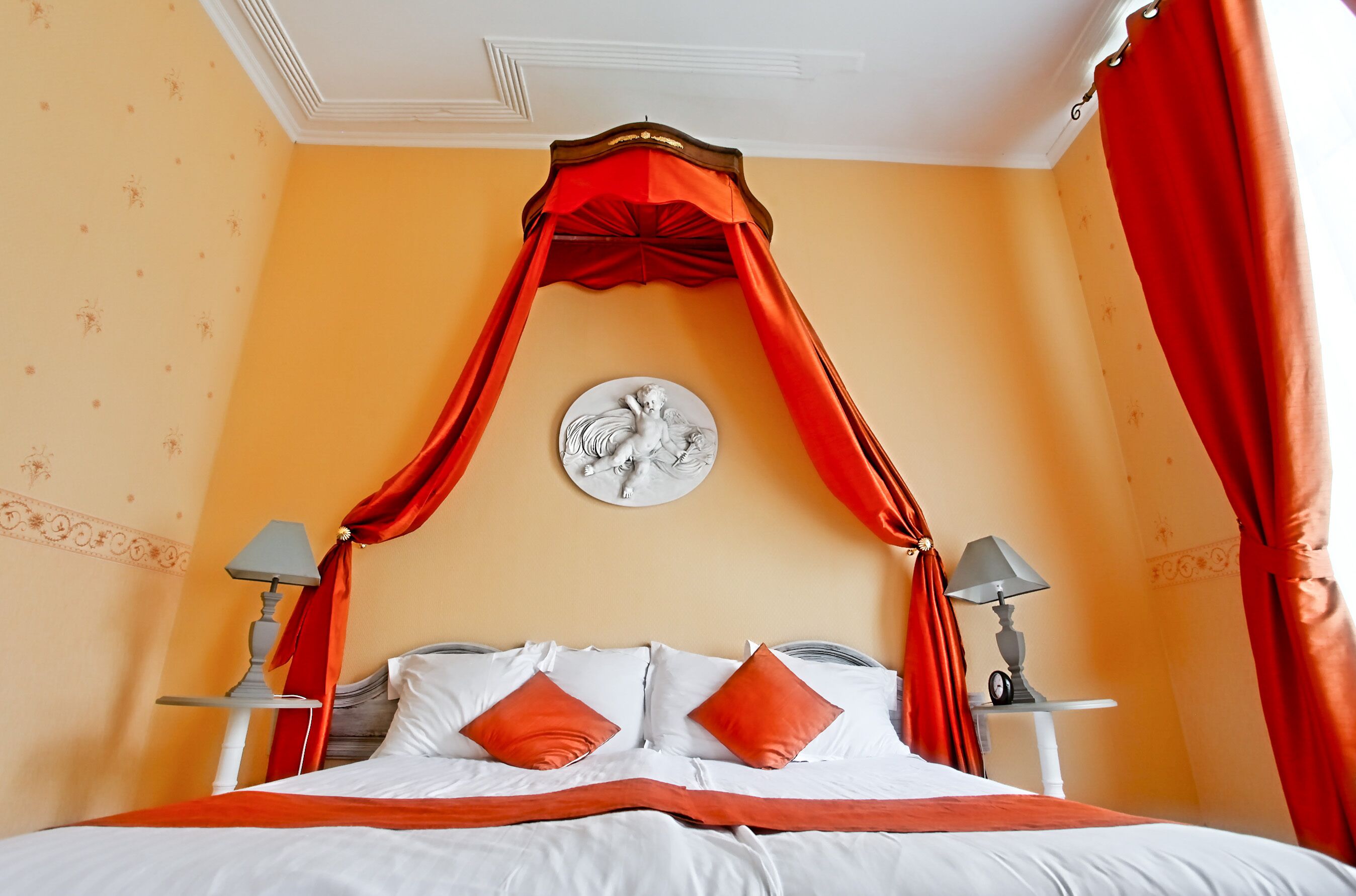Un dormitorio con cama a dosel, dos mesitas de noche con lámparas y un adorno en la pared.