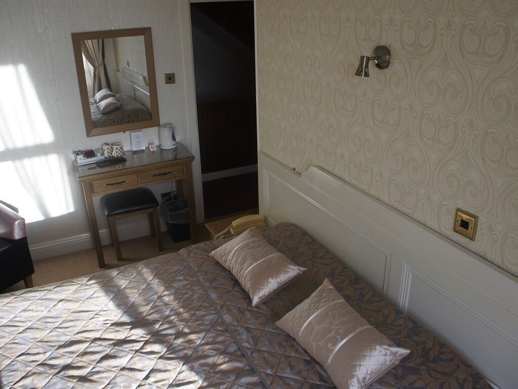 A bedroom with a bed, a desk, a chair, a mirror, and a patterned wall.