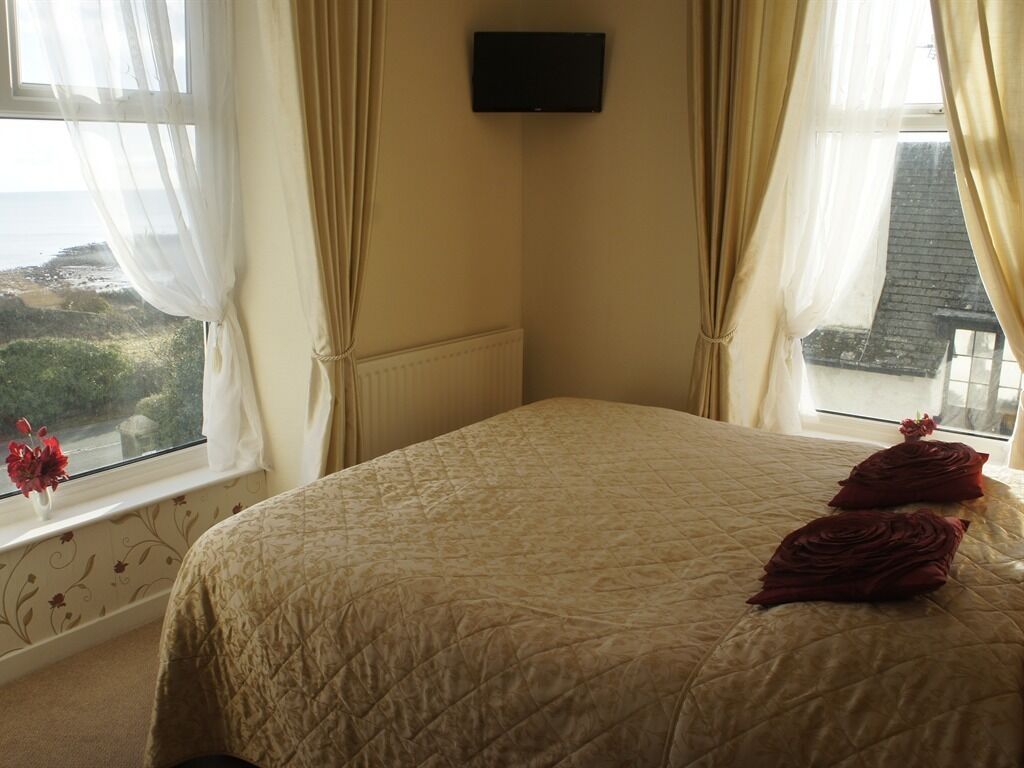 A bedroom with a bed, curtains, a TV, and a view of the sea.