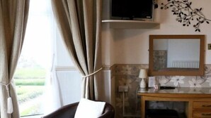 Una stanza con vista su un giardino, una scrivania in legno con uno specchio, una sedia e una televisione a parete.