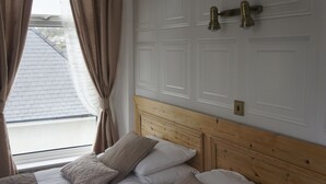 Una camera d'albergo con una testiera in legno, un letto con biancheria da letto bianco e beige e una finestra con tende.