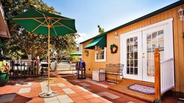 A patio area with a checkered floor, a green umbrella, and a wooden building with a white door and windows. - Old Irish Inn (Denton)