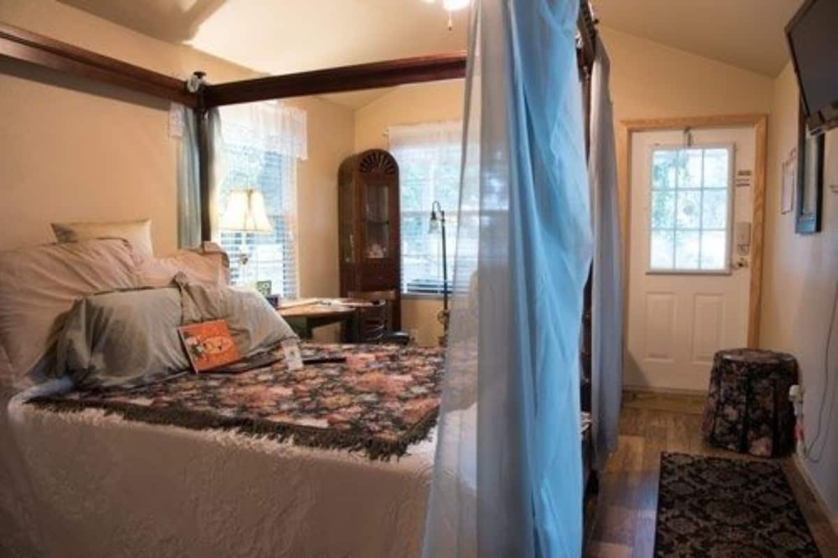 A bedroom with a bed, a desk, a chair, a lamp, a clock, and a door.