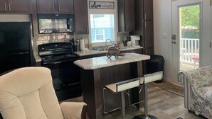 A kitchen with dark wood cabinets, a stainless steel stove, a microwave, and a bar area with stools. - Old Irish Inn (Denton)