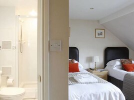 A hotel room with a shower, a toilet, two beds with pillows, and a nightstand with a lamp.