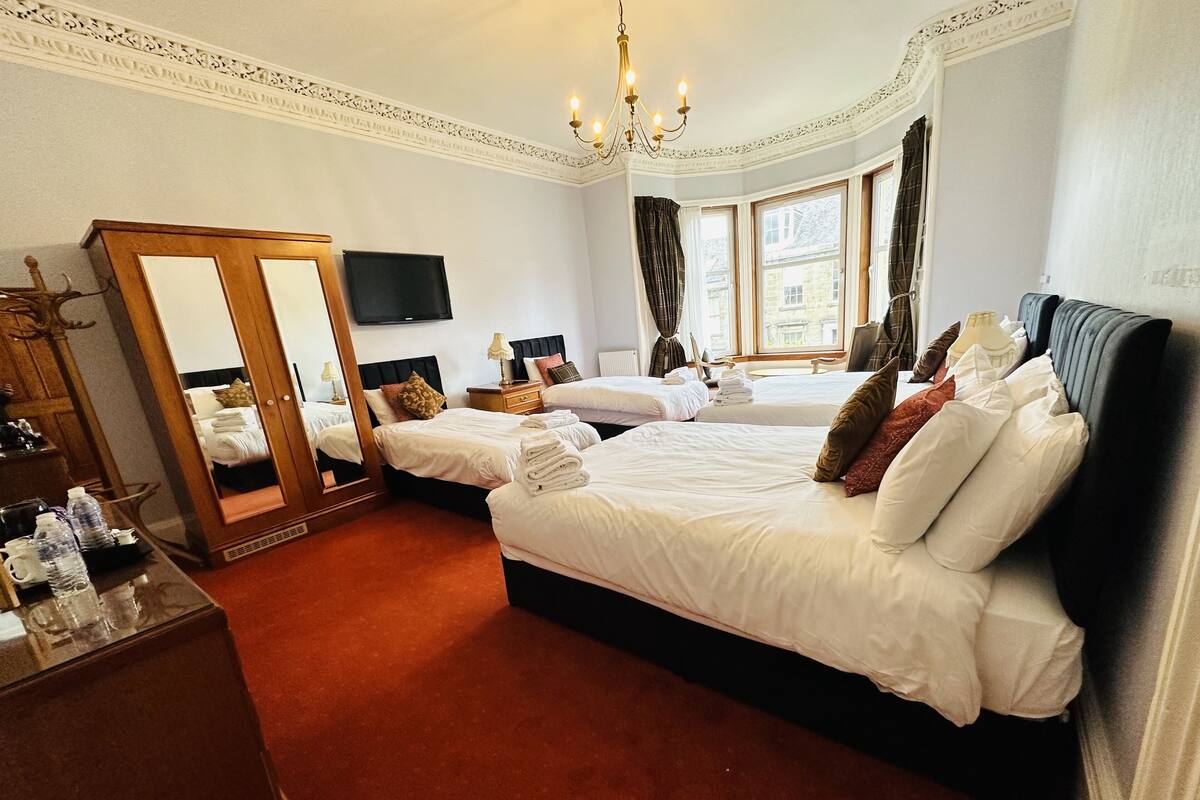 A hotel room with two beds, a large mirror, a television, and a view of the outside through a window.