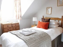 A bedroom with a bed, a nightstand, a lamp, and a window with curtains.