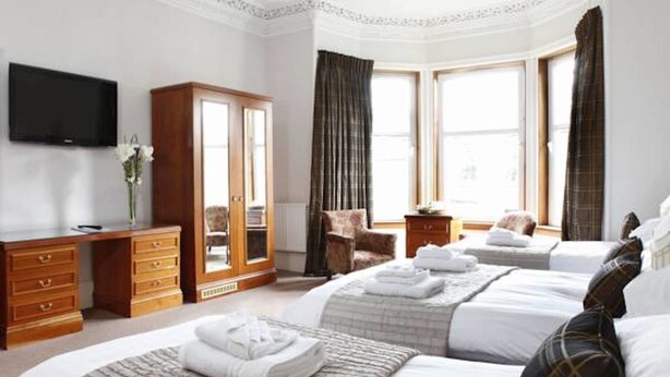 A hotel room with two beds, a wooden wardrobe, a television, and large windows with curtains. - Abbotsford Guest House (Edinburgh)