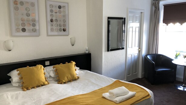 A hotel room with a bed, two wall-mounted light fixtures, a mirror, a chair, and a small table with a plant.