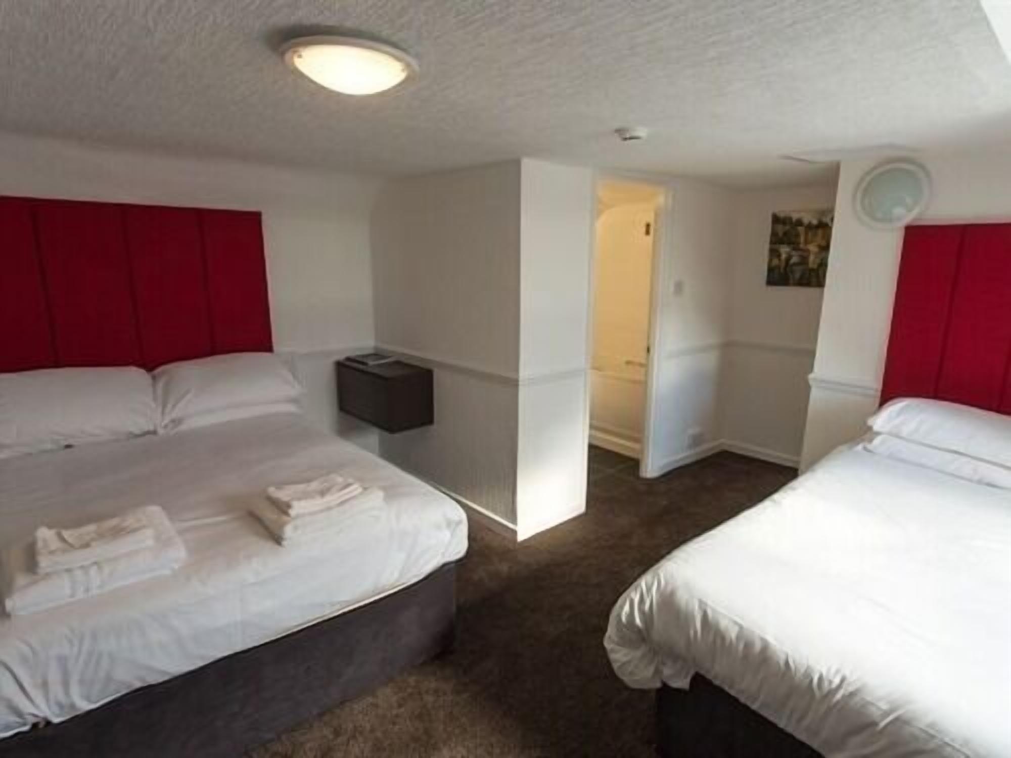 Habitación de hotel con dos camas, una mesita de noche y una lámpara de techo.