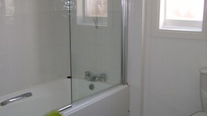 A bathroom with a glass-enclosed shower, a toilet, and a green towel on the floor.