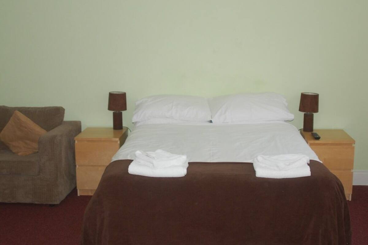 Uma cama bem arrumada com lençóis brancos, duas luminárias de cabeceira, um cobertor marrom e um travesseiro marrom sobre uma mesa de cabeceira de madeira.