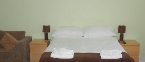 A neatly made bed with white linens, two bedside lamps, a brown blanket, and a brown pillow on a wooden nightstand.