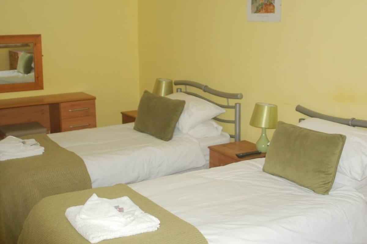 Quarto de hotel com duas camas de solteiro, cada uma com travesseiro e mesa de cabeceira com abajur.