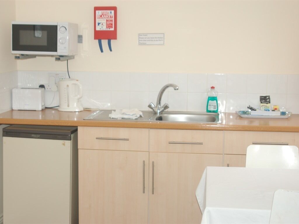 Una kitchenette compacta equipada con microondas, tostadora, tetera, lavabo y escurreplatos.