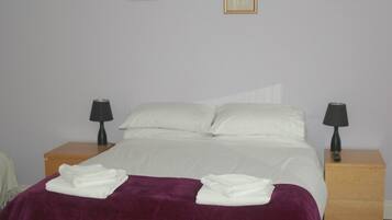 A neatly made bed with white linens, a purple blanket, and two bedside lamps on wooden nightstands.