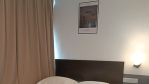 Una habitación de hotel con una cama grande, un cabecero, una mesita de noche y una lámpara fijada a la pared.