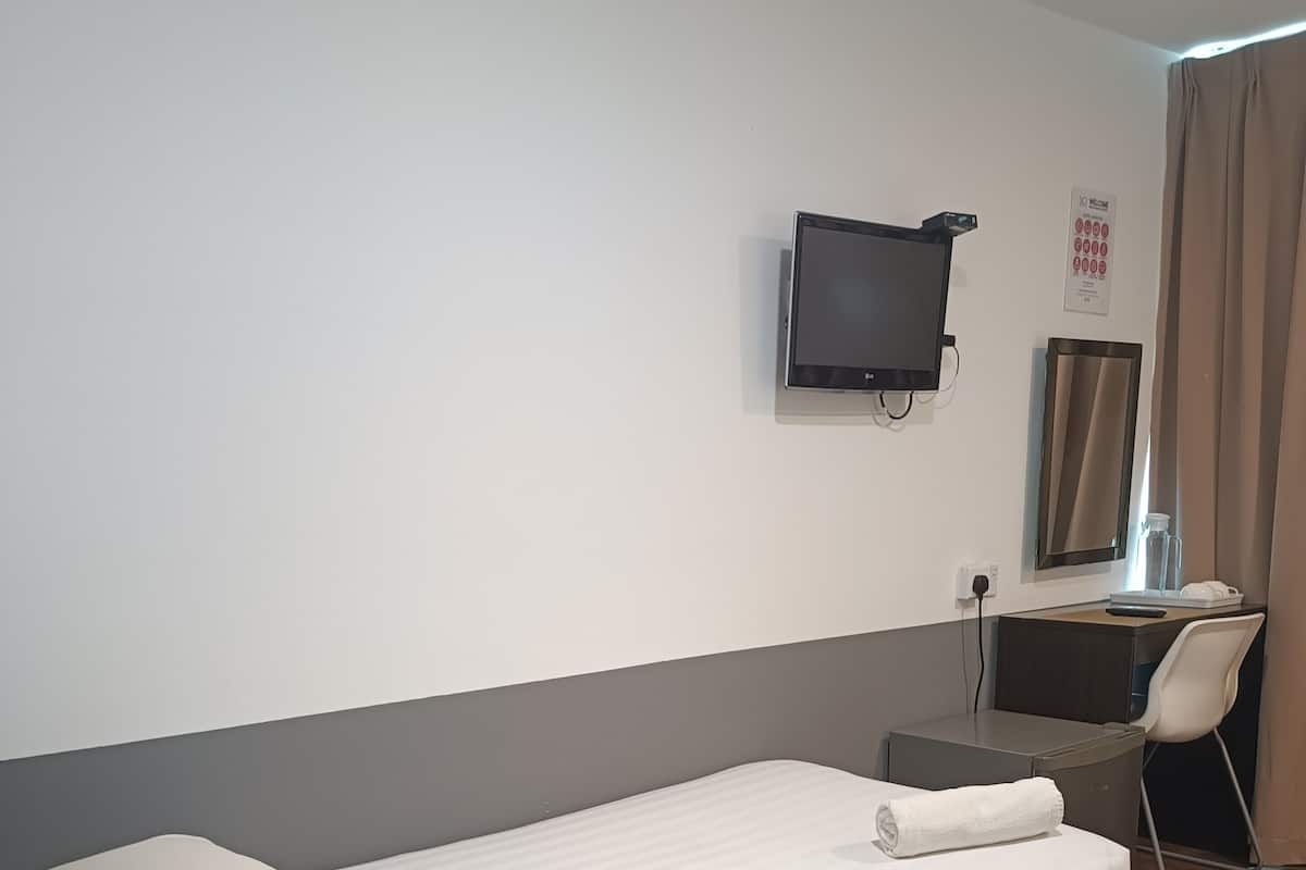 A hotel room with a single bed, a desk, a chair, a television mounted on the wall, and a mirror.