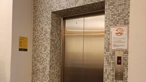 Un ascensor con detalles metálicos, un revestimiento de mosaicos y un cartel de prohibido fumar.