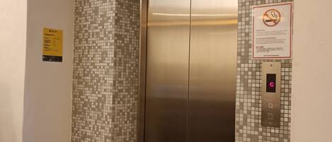 An elevator with a metallic finish, a mosaic tile wall, and a no-smoking sign.
