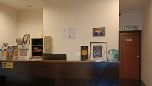Un mostrador de recepción con detalles en madera oscura, un cartel que indica disponibilidad de WiFi y una puerta con la etiqueta "KELUAR".