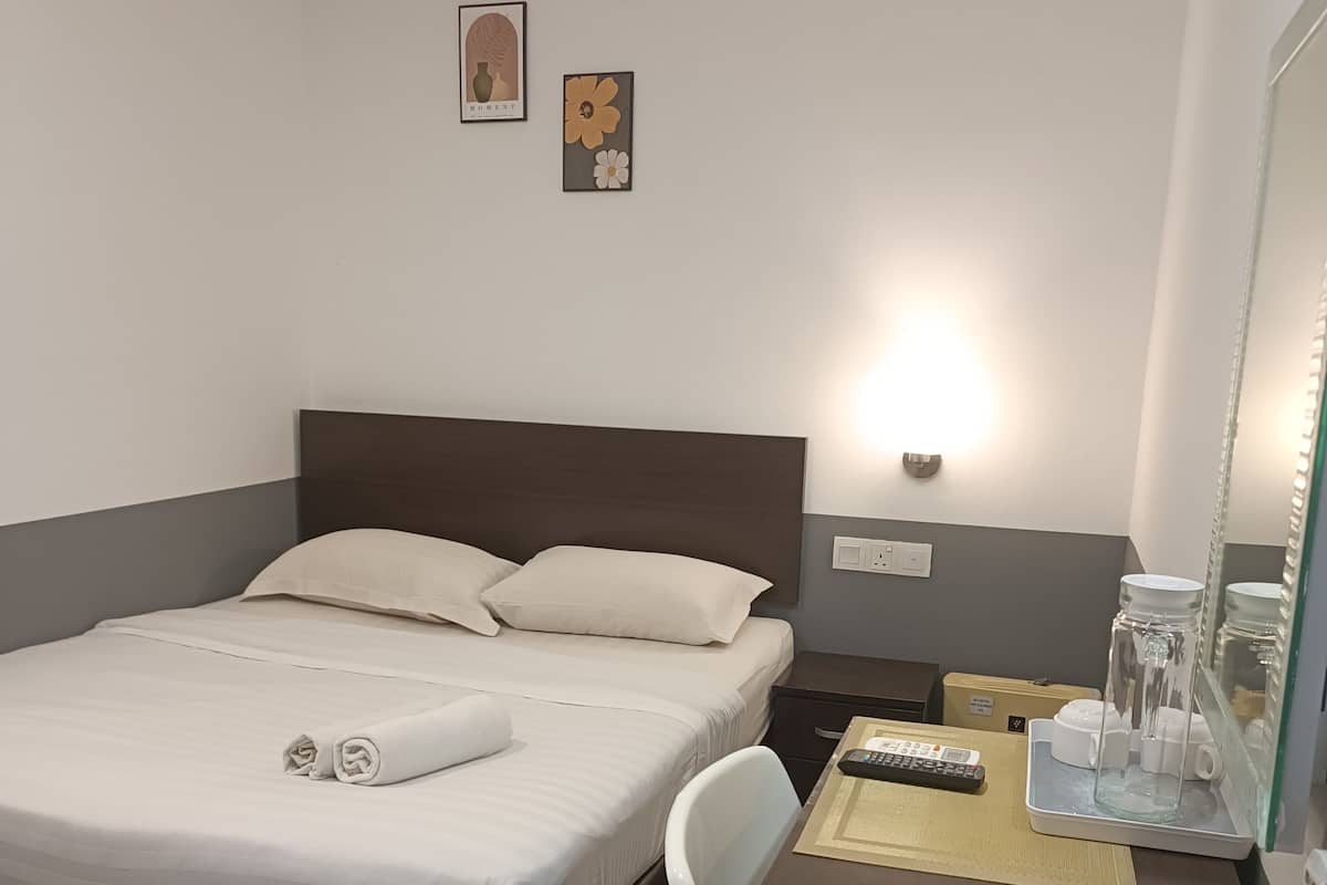 A hotel room with a bed, bedside table, and a desk with a chair. There are two wall-mounted light fixtures and a mirror.