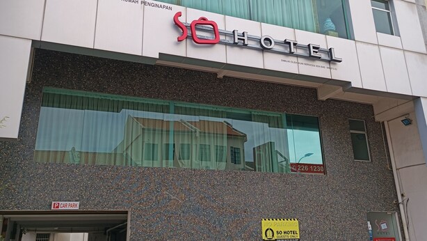 Un hotel con fachada moderna, entrada visible y señalización que indica un estacionamiento.