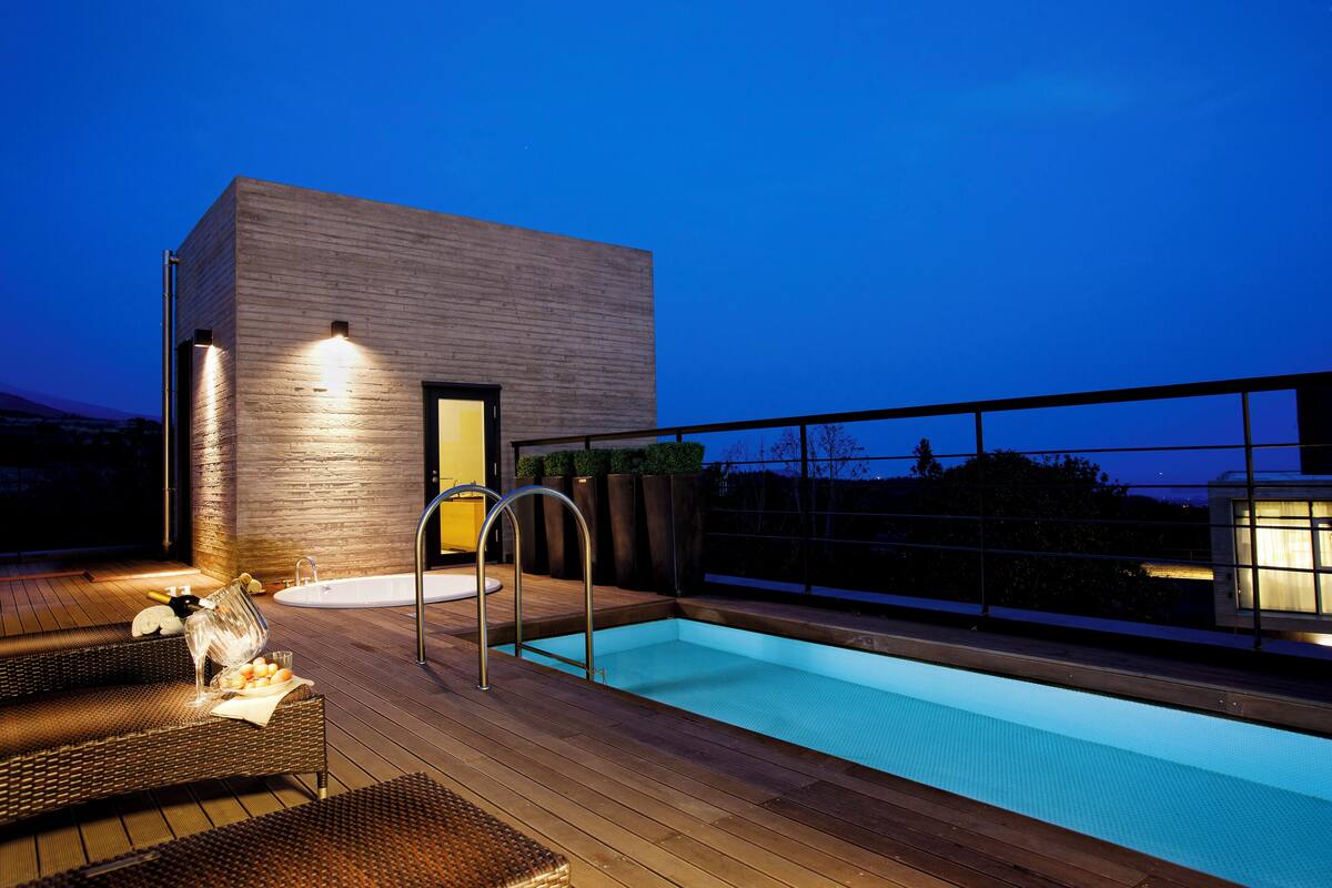 A modern outdoor pool area with a wooden deck, a built-in hot tub, and a glass-enclosed jacuzzi.