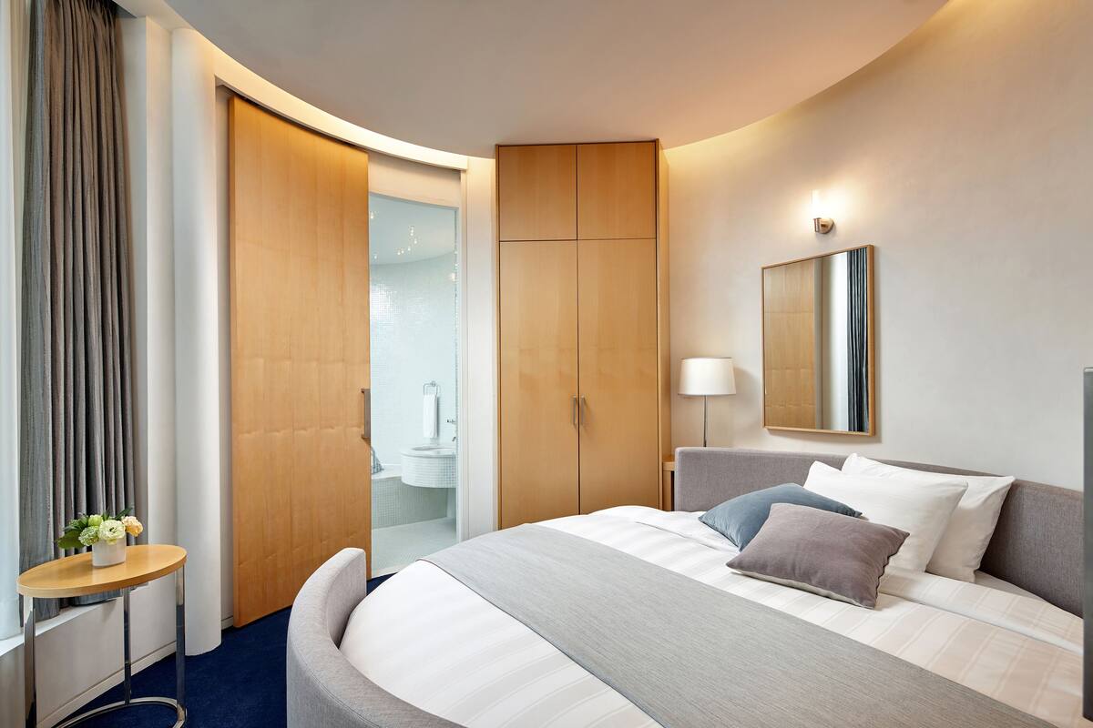 A hotel room with a large bed, a bedside table, a mirror, and a wardrobe.