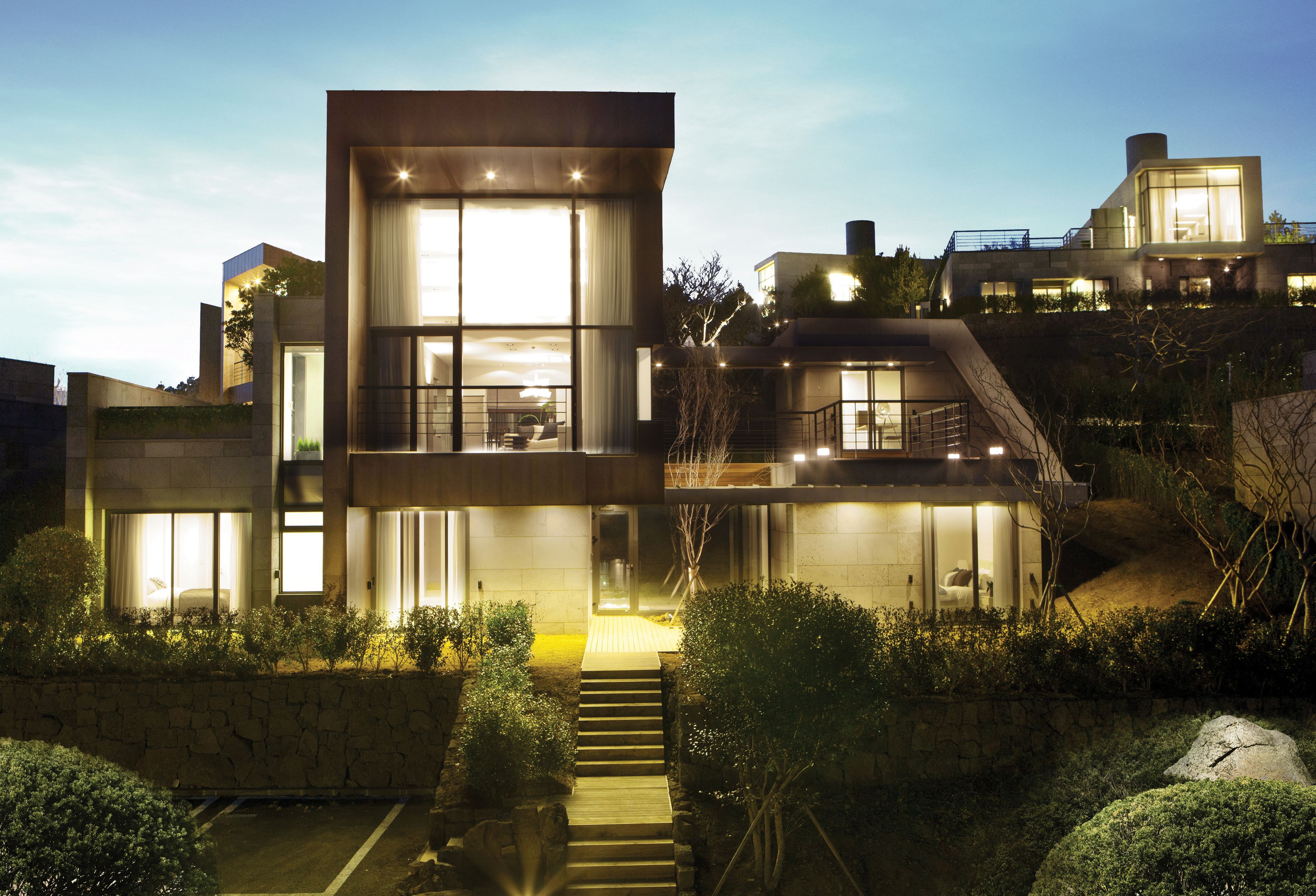 A modern multi-story house with large windows, a staircase, and a well-lit exterior.