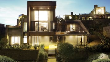 A modern multi-story house with large windows, a staircase, and a well-lit exterior.