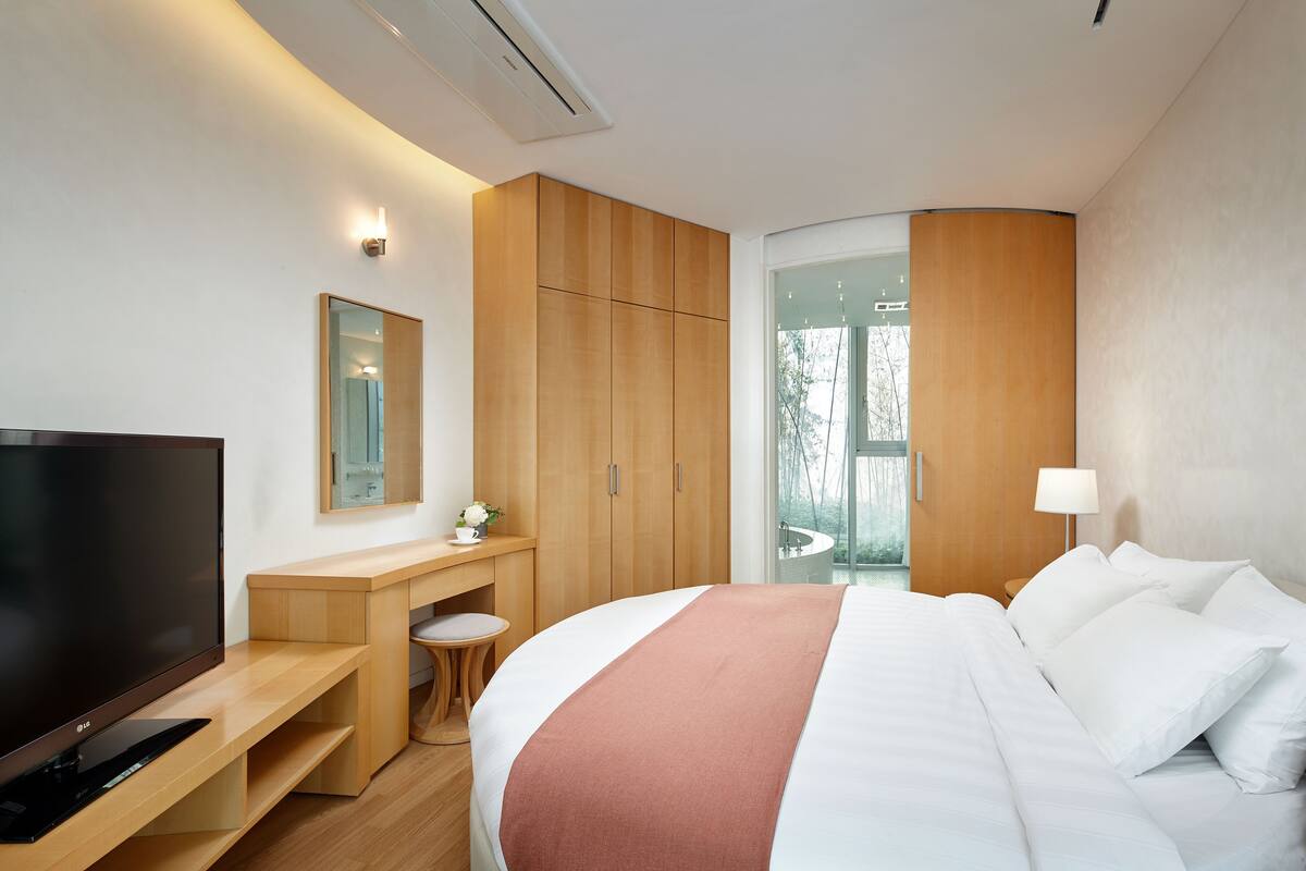 A modern hotel room with a large bed, a TV, a desk, and a wardrobe.