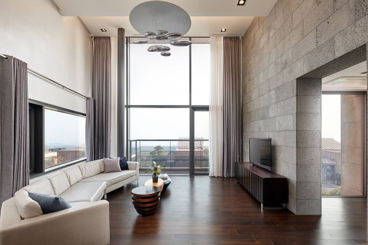 A modern living room with a large window, a sofa, a coffee table, and a flat-screen TV.