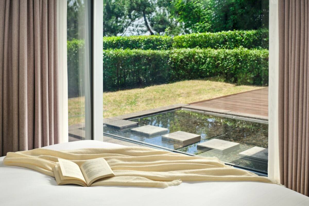 A bedroom with a large window, a bed, and an open book.