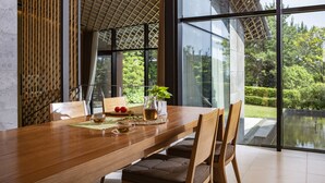 Un comedor moderno con una mesa de madera, sillas y vistas a un jardín a través de amplios ventanales.