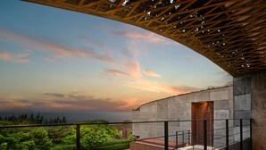 Un balcón con vista al atardecer sobre el océano, un muro de piedra y una pérgola de madera.