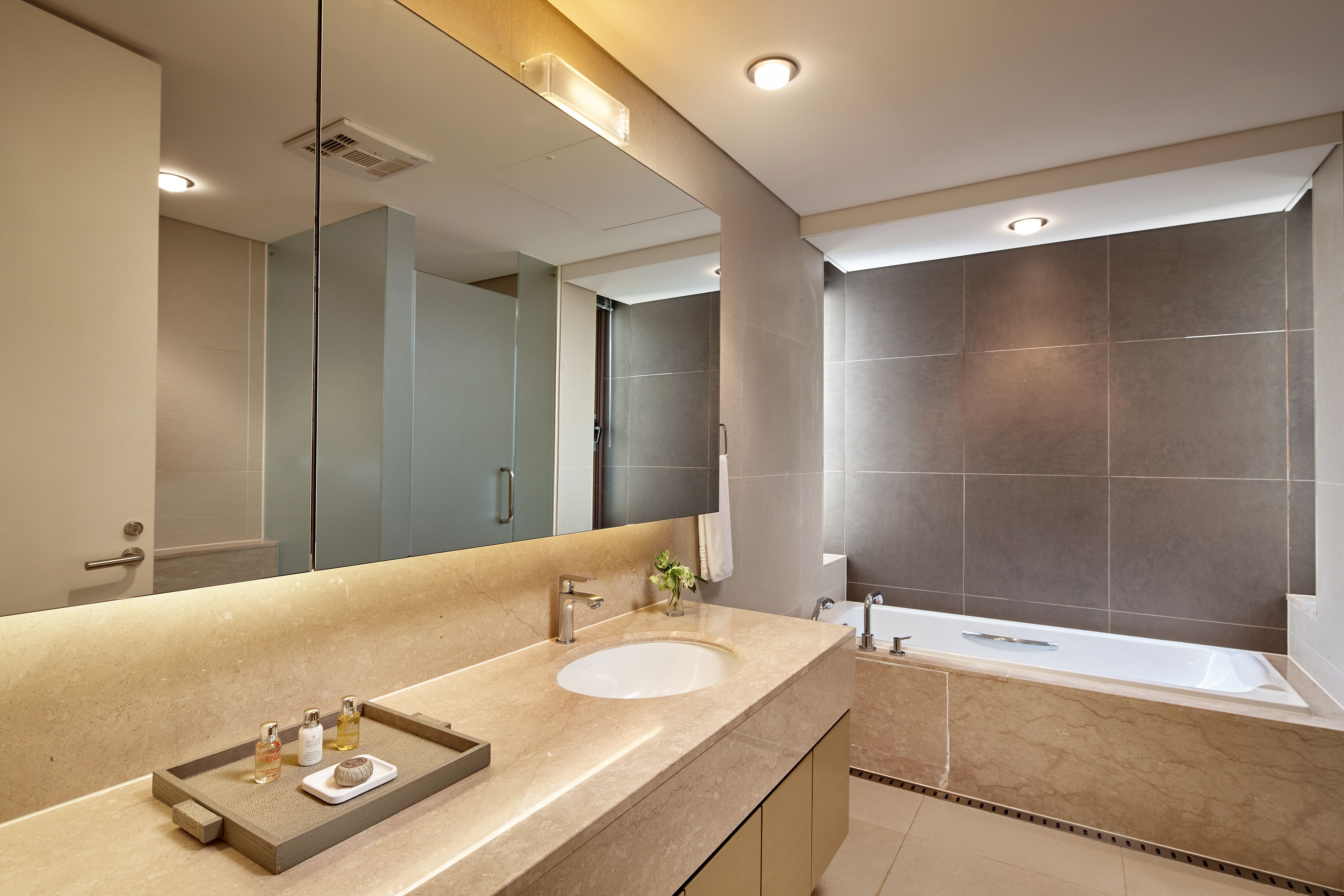 A modern bathroom with a large mirror, a sink, and a bathtub.