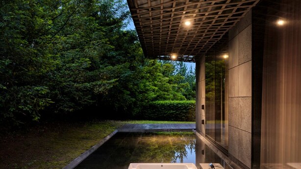 Un área de spa con un jacuzzi, una terraza de madera y un muro de vidrio con vistas a un jardín.