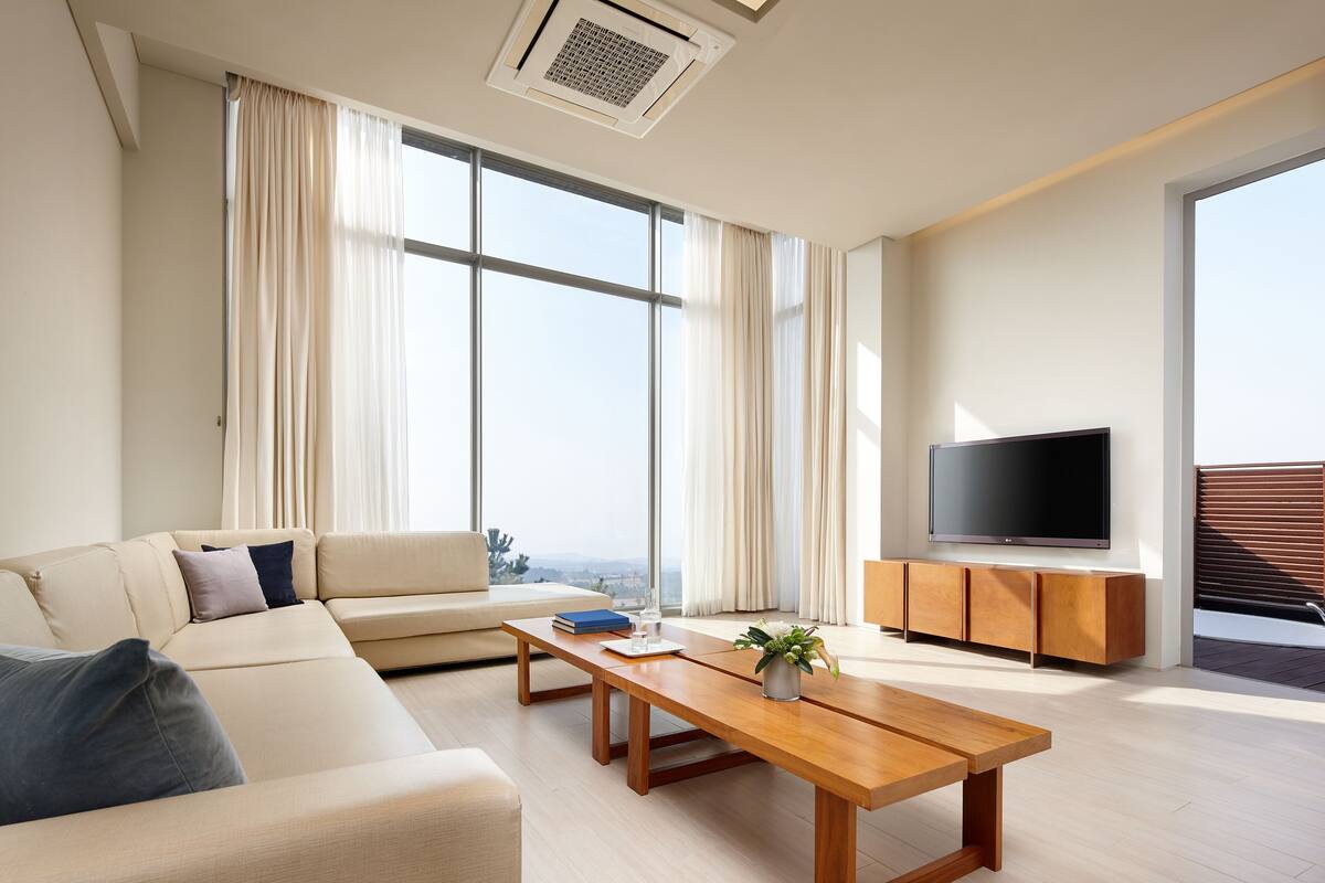 A modern living room with a sofa, a coffee table, a TV, and a large window with curtains.