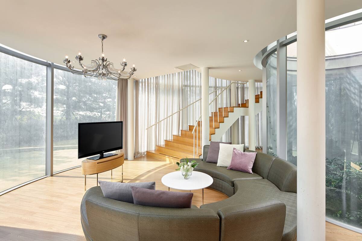 A modern living room with a curved sofa, a flat-screen TV, and a chandelier.