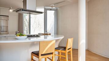 A modern kitchen with a white island, two wooden chairs, a bowl of fruit, and a window providing natural light.