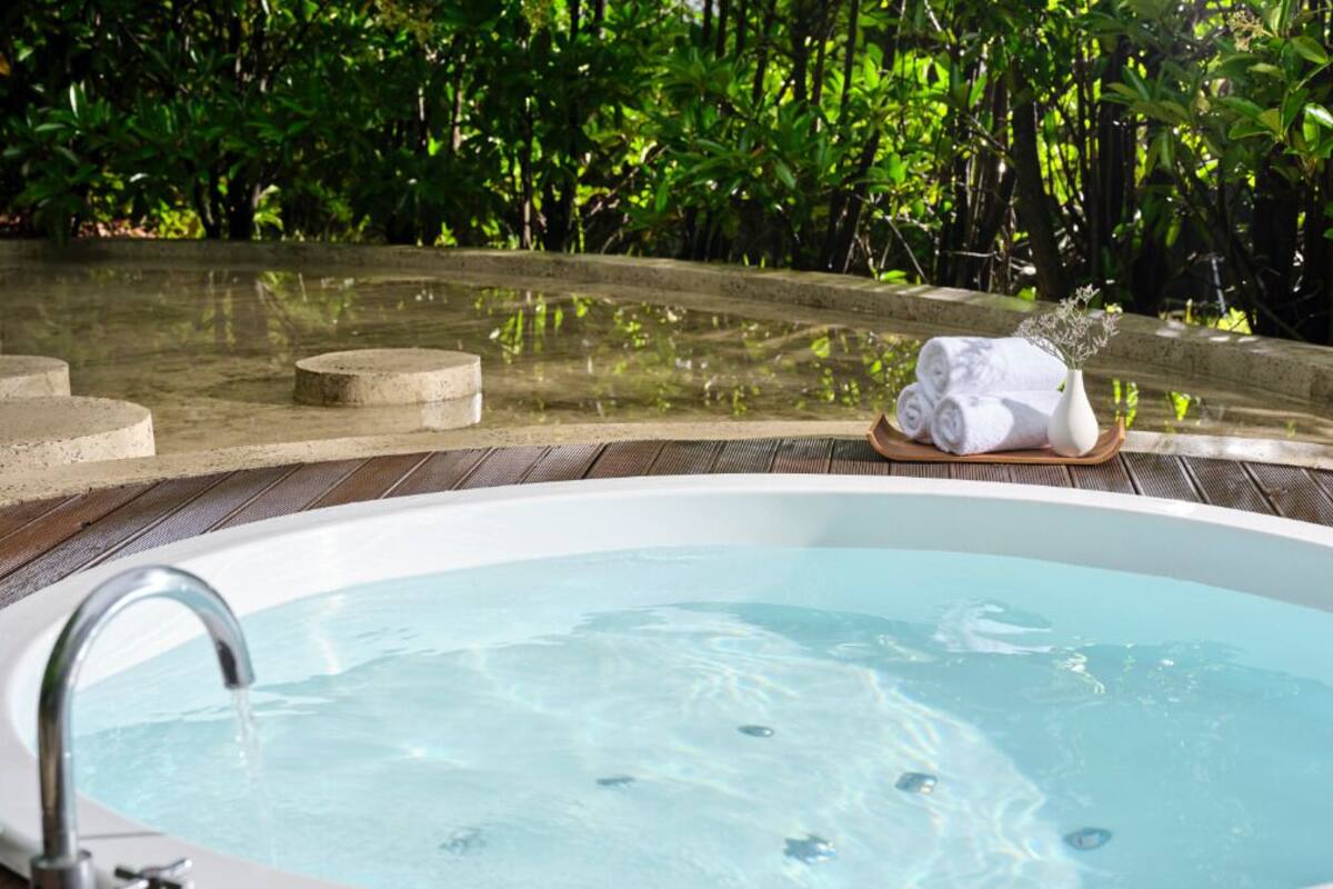 A hot tub with a wooden deck, surrounded by lush greenery.